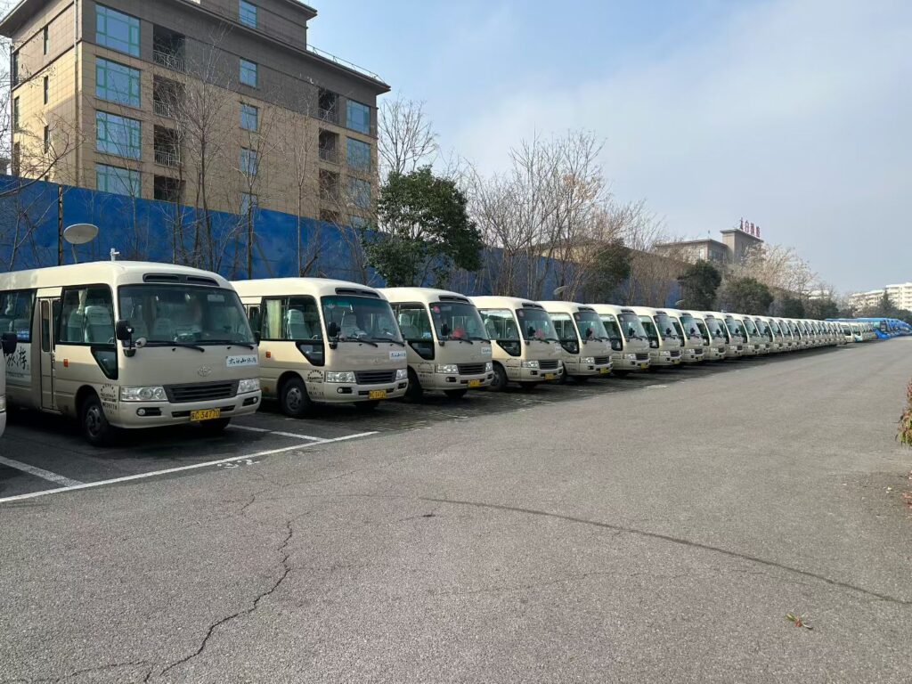 A massive fleet of uniform beige used Toyota Coaster minibuses lined up in an organized outdoor parking lot in China. The image showcases a large inventory of well-maintained 23-30 seater buses ready for international export. This illustrates our capacity for bulk fleet orders and consistent vehicle quality.